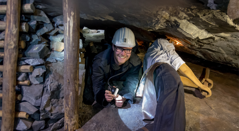 Arbeiter in einem Bergwerk unter Tage, mit Helm und Werkzeug, in dunkler Umgebung.