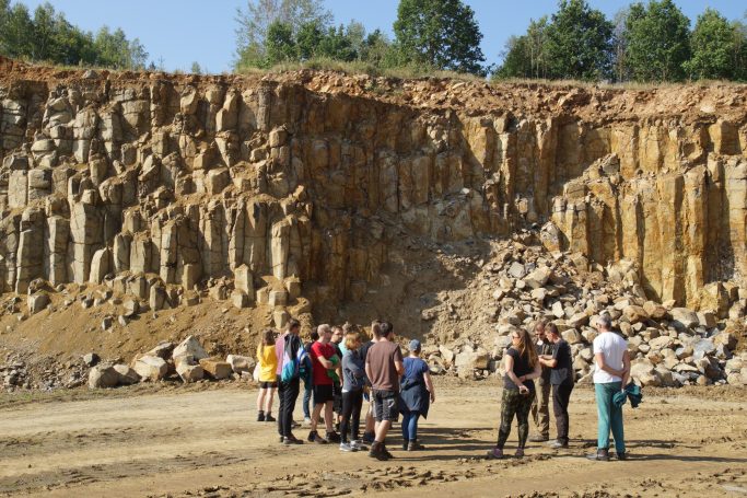 Gruppe von Menschen steht vor einer geologischen Felswand in einem Steinbruch.