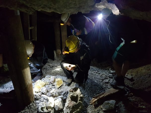 Personen erkunden eine dunkle Höhle mit Taschenlampen und Helmen.